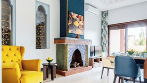 A living room with a yellow armchair, a fireplace, and a dining area with a table and chairs. - Domaine Mandar Atlas (Marrakech)