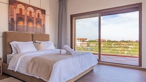 A bedroom with a large bed, a view of a building through the window, and a balcony with a railing. - Domaine Mandar Atlas (Marrakech)