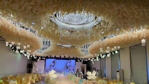 Un salón de banquetes con una larga mesa dispuesta para un evento formal, decorado con flores blancas y una lámpara de araña central.