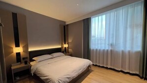 Una habitación de hotel moderna con una cama grande, lámparas de noche, una mesita de noche y vistas al exterior a través de cortinas traslúcidas.