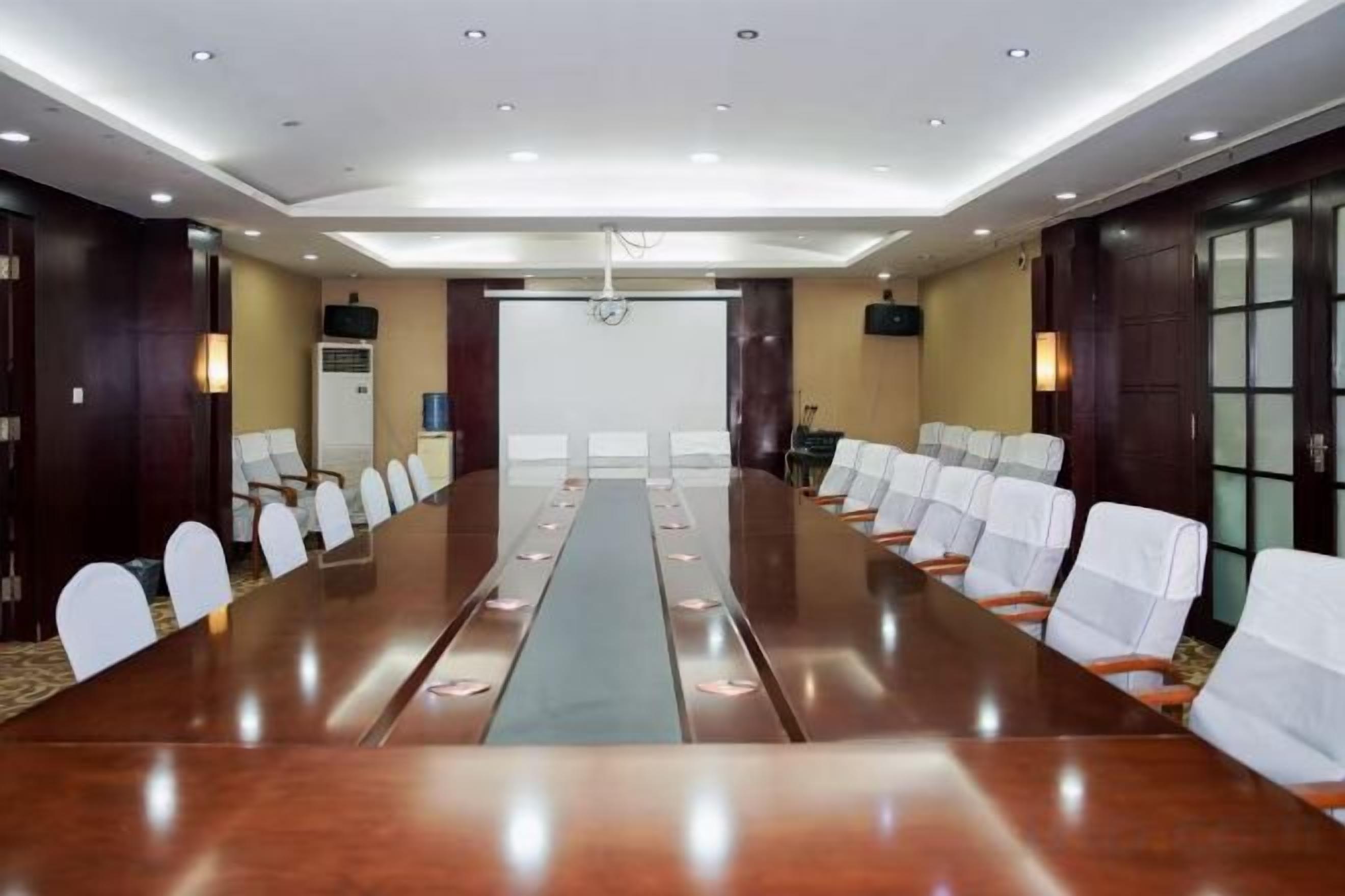 A conference room with a long table, chairs, and a projector screen.