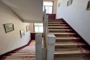 A staircase with a patterned carpet and a handrail, leading to a landing with framed pictures on the wall.