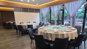 Un salón de conferencias con una mesa de vidrio rodeada de sillas, ventanas amplias con cortinas y piso de baldosas.