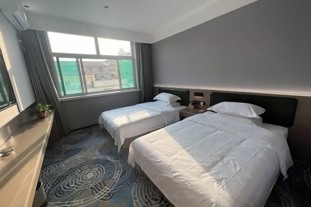 A hotel room with two beds, a dresser, a window with curtains, and a patterned carpet.