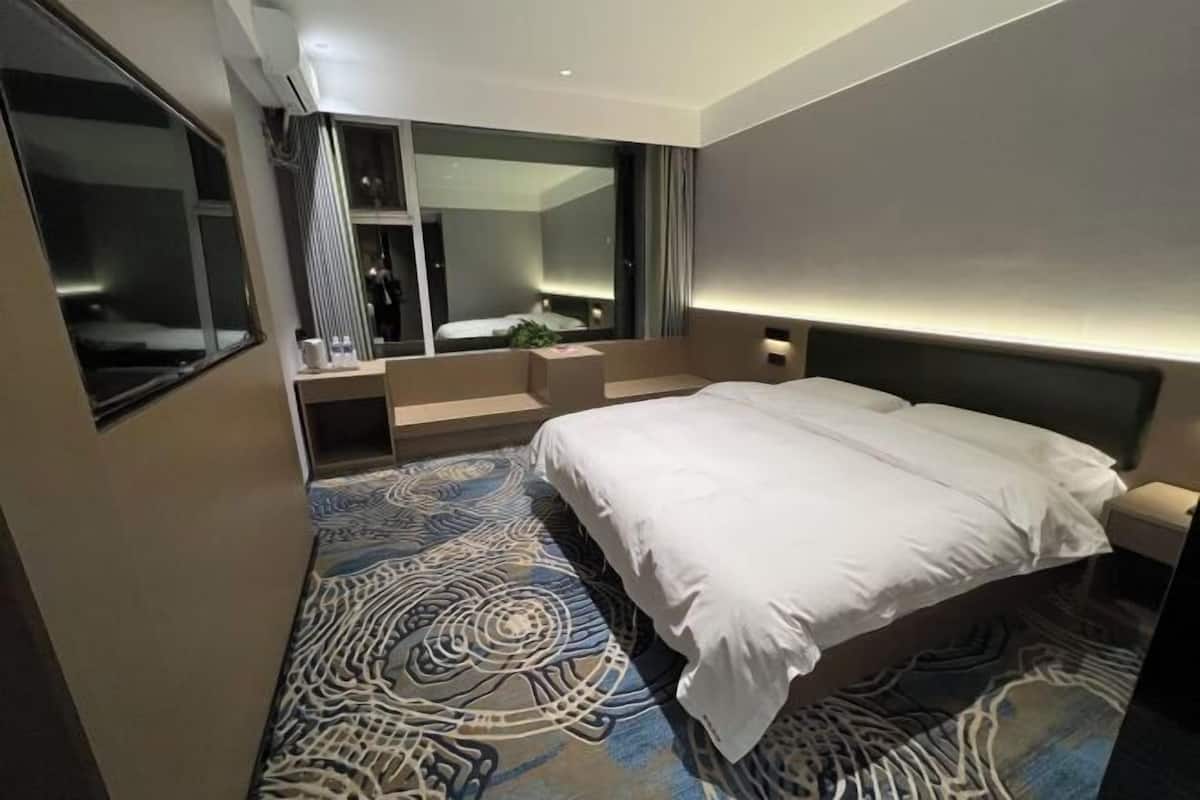 A modern hotel room with a large bed, a built-in desk, and a large mirror.