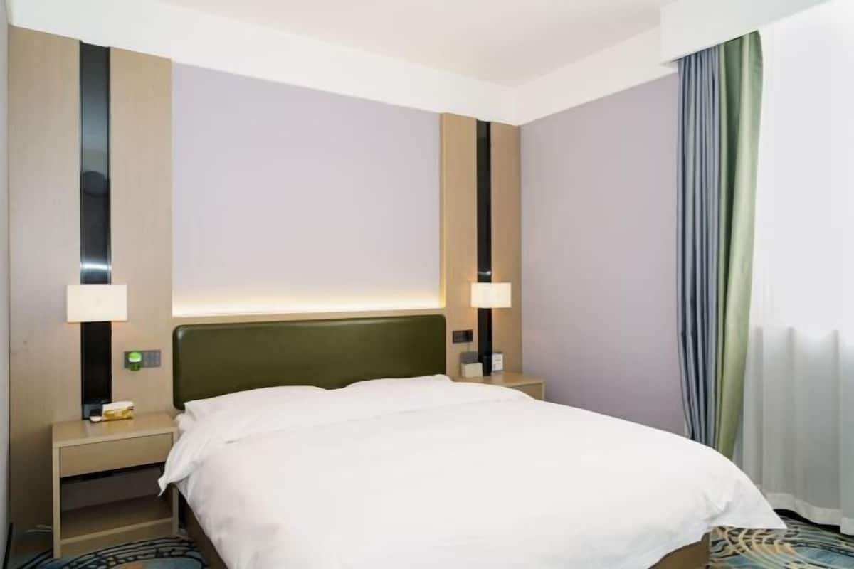A hotel room with a bed, bedside tables, lamps, and a curtain.