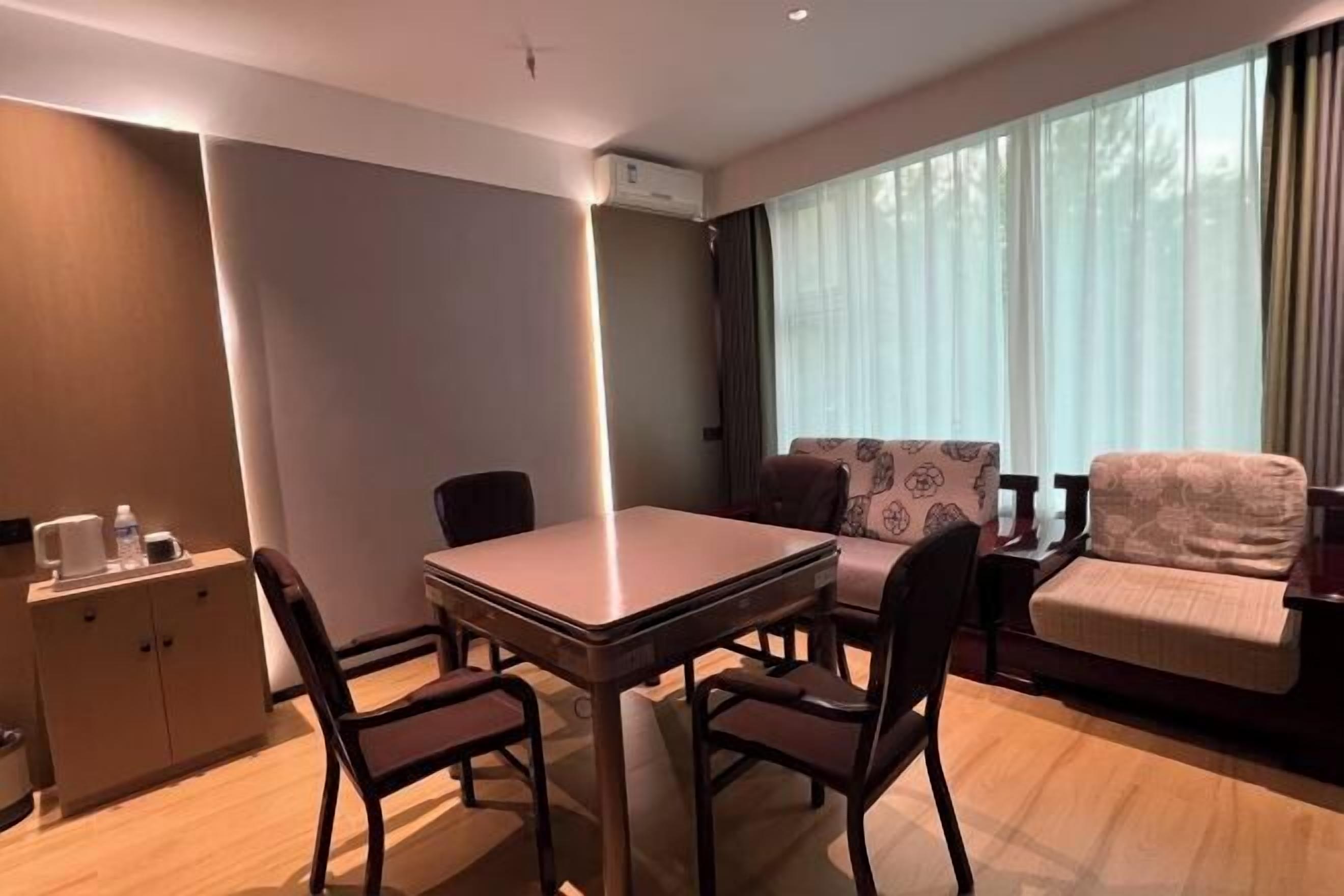A modern hotel room with a dining table, chairs, a sofa, and a cabinet.