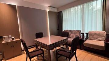 A modern hotel room with a dining table, chairs, a sofa, and a cabinet.