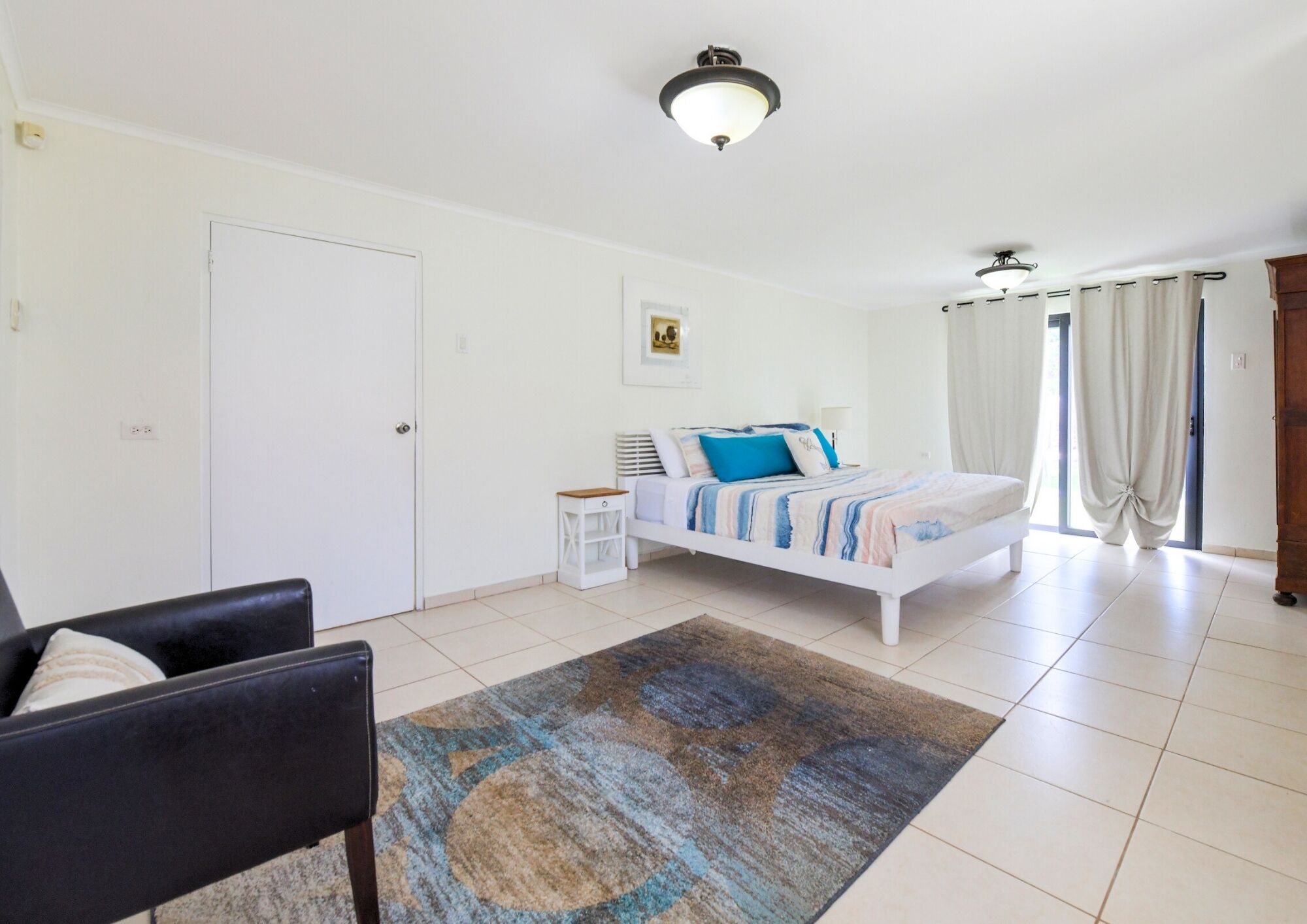 Une chambre à coucher comprenant un lit, une chaise, une table de chevet, un tapis et un luminaire au plafond.