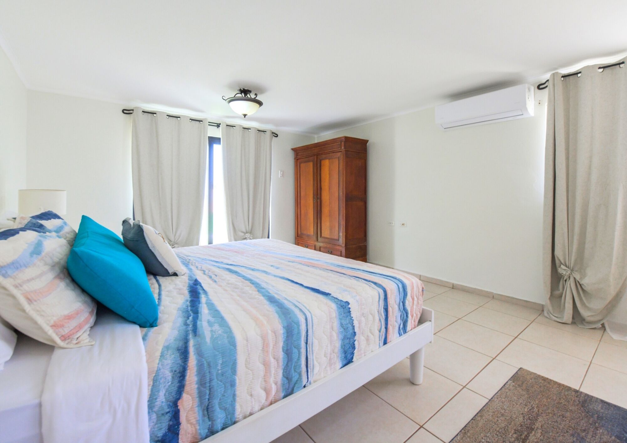 Un dormitorio con cama, cortinas, armario y aire acondicionado.