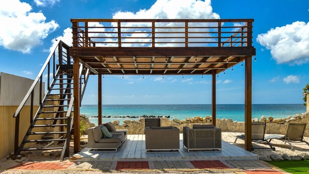 Ein überdachter Außenbereich mit einer Holz-Pergola, einer Treppe und Blick auf den Ozean.