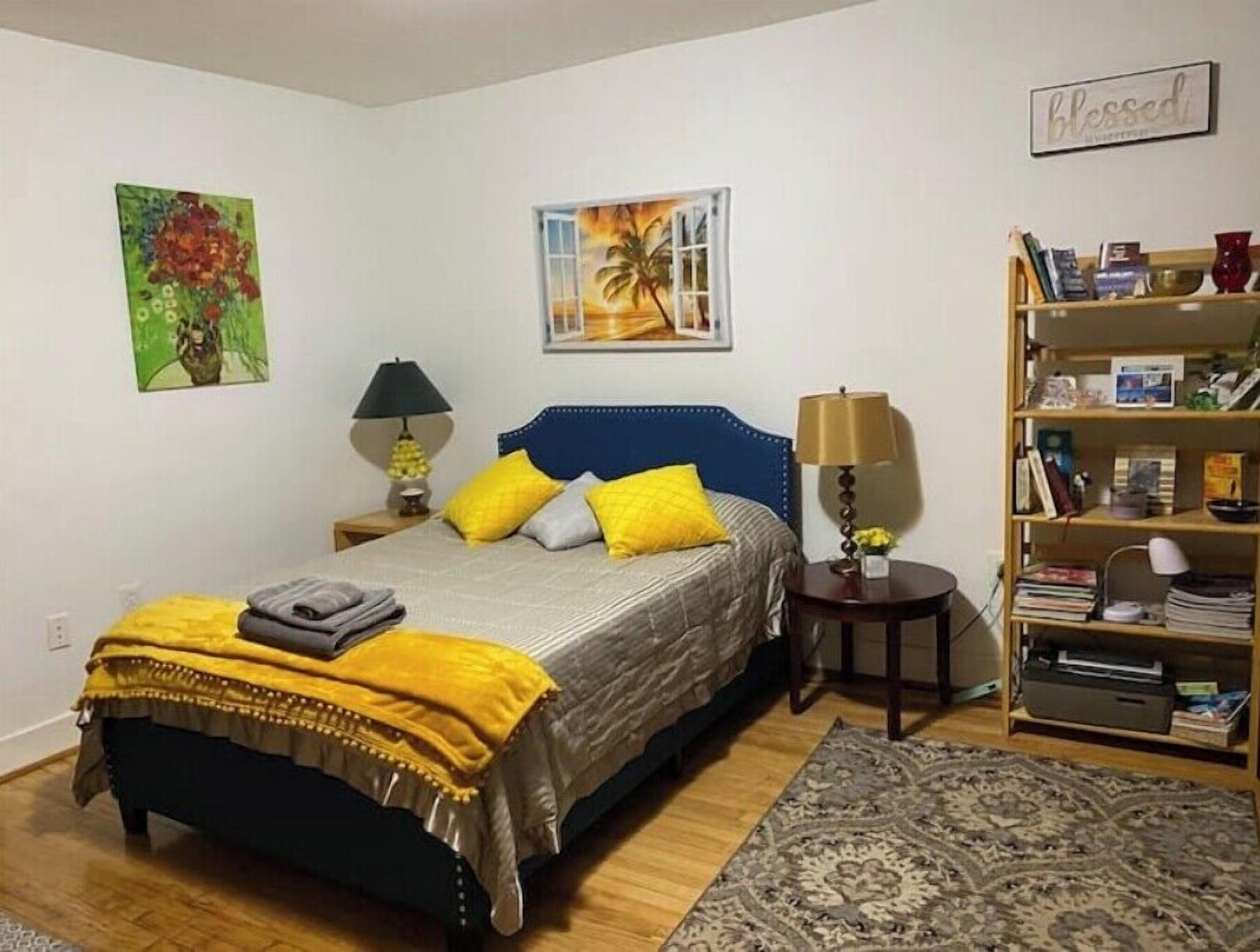 A bedroom with a bed, a nightstand, a bookshelf, and two wall art pieces.