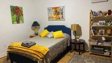 A bedroom with a bed, a nightstand, a bookshelf, and two wall art pieces.