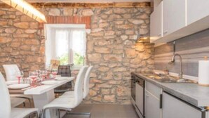 Una cucina moderna con pareti in pietra, mobili bianchi e un'area pranzo con sedie e tavolo apparecchiati per un pasto.