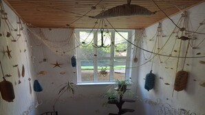 A room with a wooden ceiling, a window with a view of greenery, and various hanging decorations.