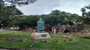 A statue on a pedestal in a park with grass and trees.