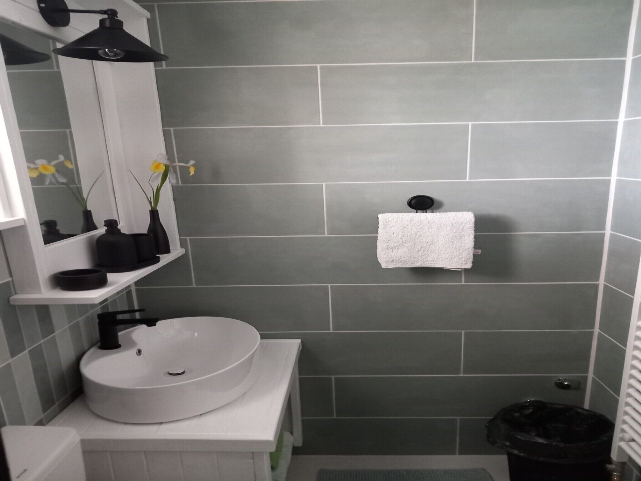 A bathroom with a white sink, a mirror, a towel rack, and a trash bin.