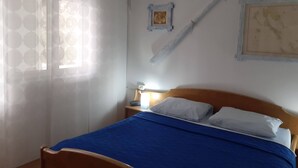 Ein Schlafzimmer mit einem Bett, einem Nachttisch, einem Wandheizkörper und einem Fenster mit gemusterten Vorhängen.
