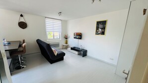 A modern living room with a sofa, a small table, a TV, and a window with blinds. - Cocooning apartment 50 m2, terrace 40 m2 (Thonon-les-Bains)