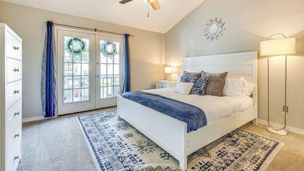 A bedroom with a bed, a ceiling fan, a nightstand, a lamp, a dresser, and a window with curtains. - Mobile Townhome Near University of South Alabama! (Mobile)