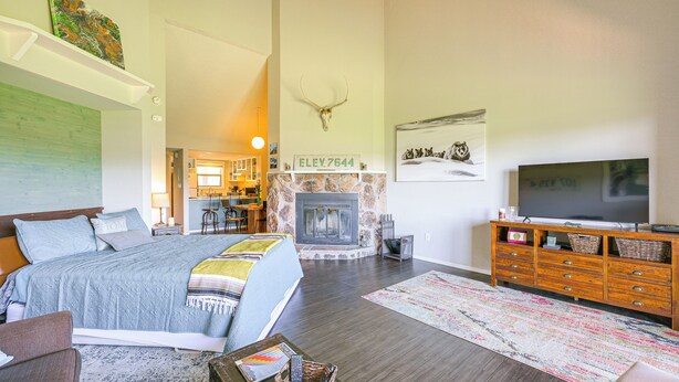 Amplia sala de estar con chimenea, una cama grande, televisor y comedor al fondo.