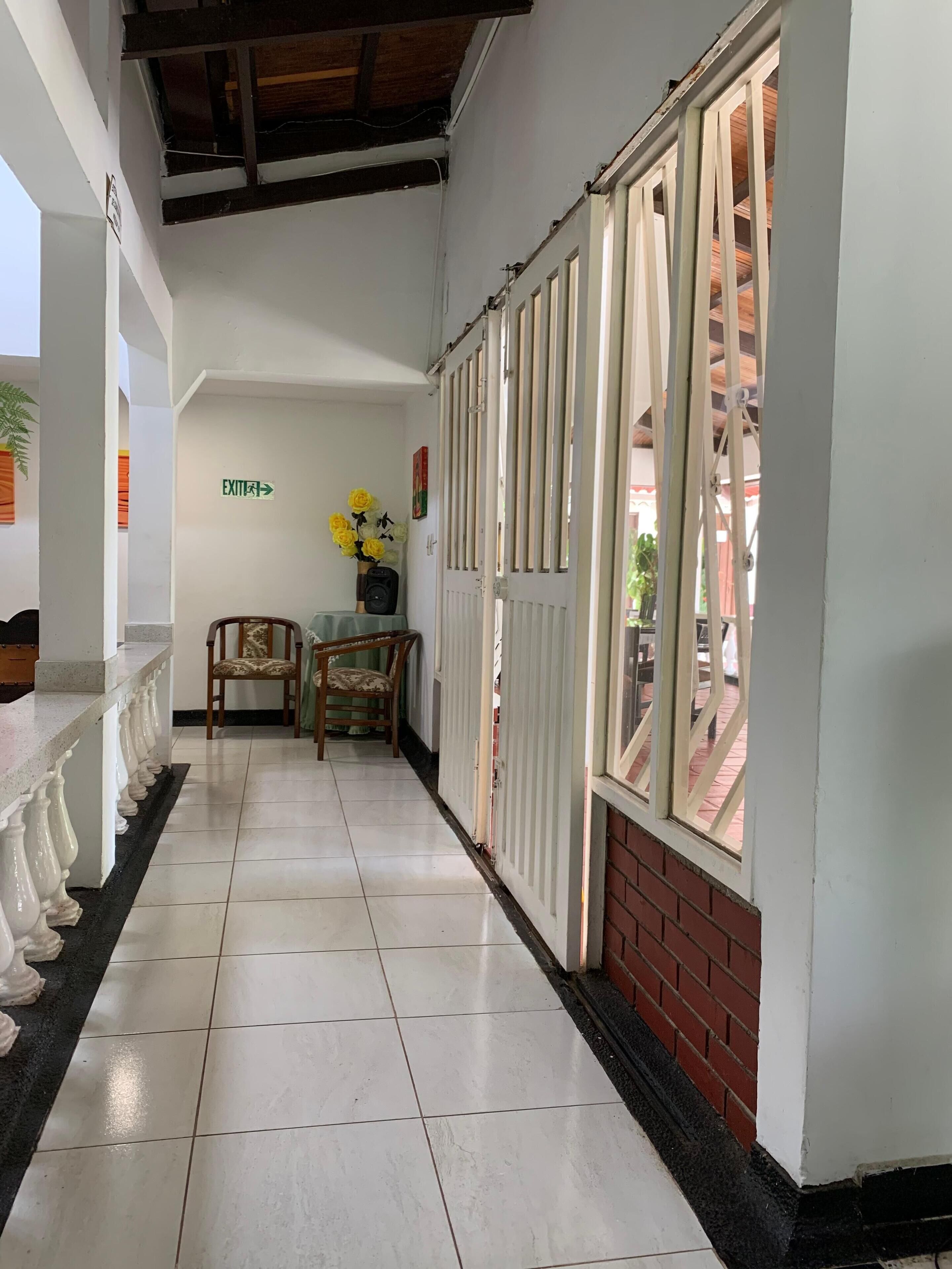 A hallway with a tiled floor, a chair, a small table with a vase of flowers, and a sign indicating an exit.
