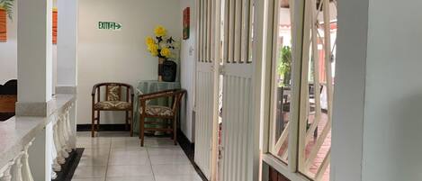 A hallway with a tiled floor, a chair, a small table with a vase of flowers, and a sign indicating an exit.