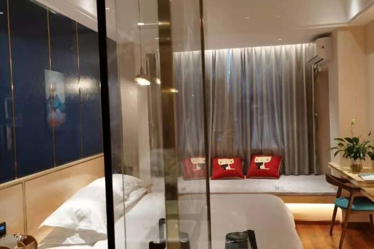 Habitación de hotel con cama, escritorio y silla, ventana con cortinas y un cartel en la pared.