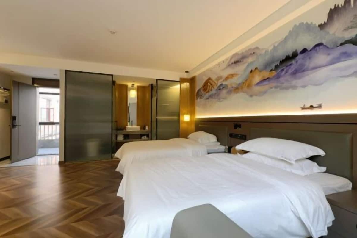 Habitación de hotel con dos camas, un cuadro grande en la pared y vistas al exterior.