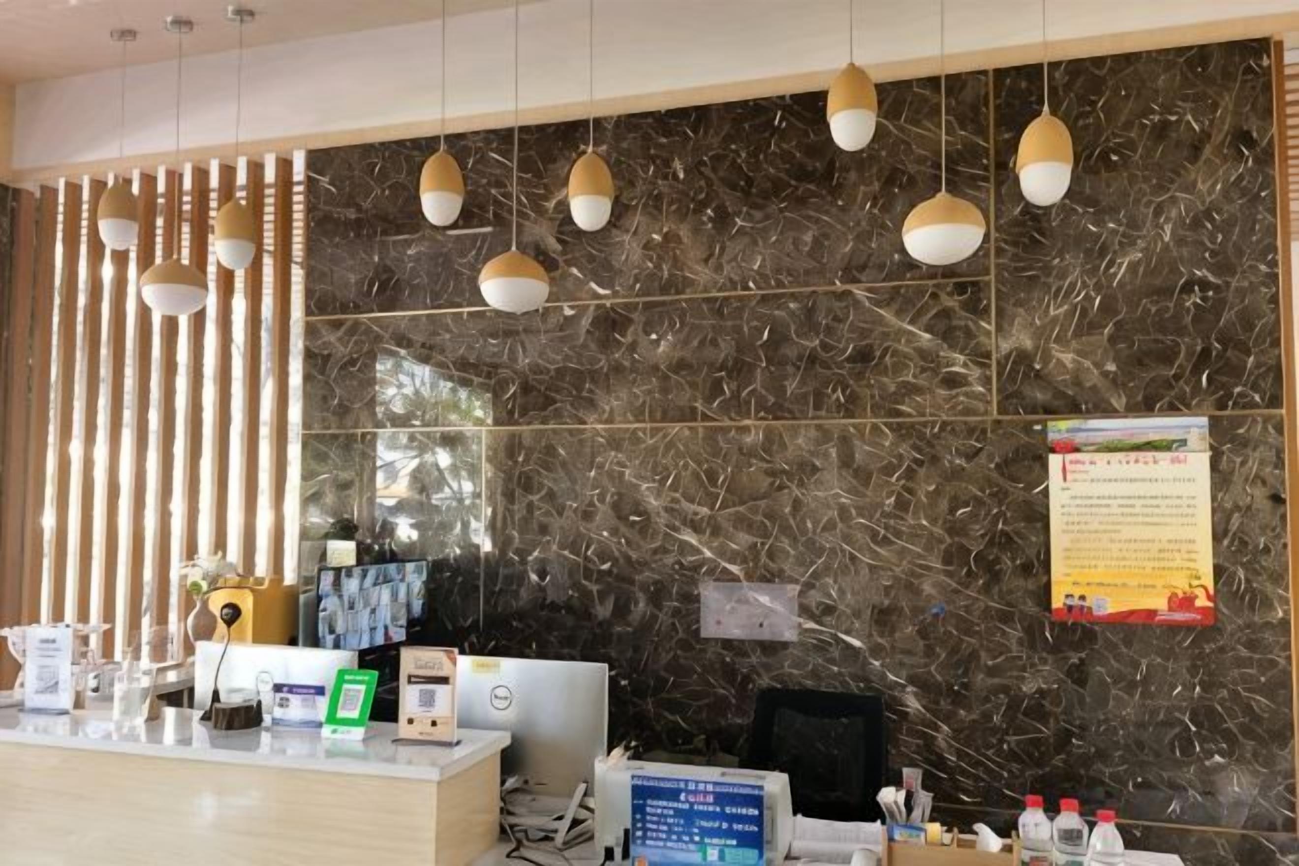 Un área de recepción con pared de mármol, lámparas colgantes, mostrador de recepción y un monitor de computadora.
