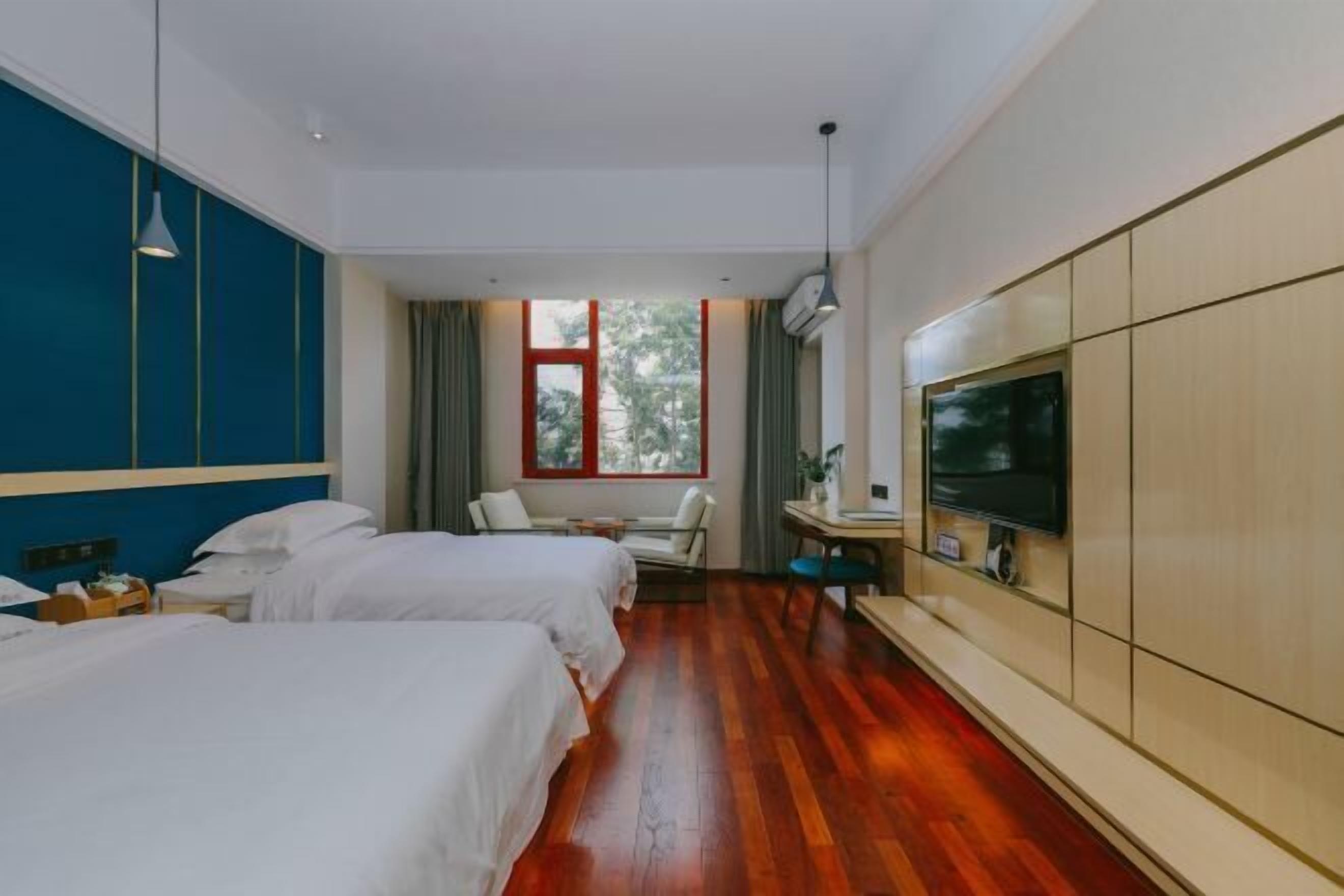 A hotel room with two beds, a desk with a chair, a TV, and a large window with curtains.