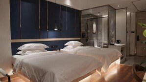 Camera d'albergo con due letti, una parete di accent in blu scuro, box doccia in vetro e pavimento in legno.