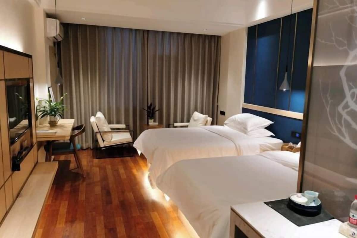 Habitación de hotel con dos camas, un escritorio, una silla, un televisor y un ventanal grande con cortinas.