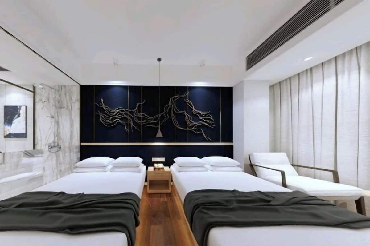 Una habitación de hotel moderna con dos camas, una obra de arte grande en la pared, una mesita de noche de madera y una silla blanca.
