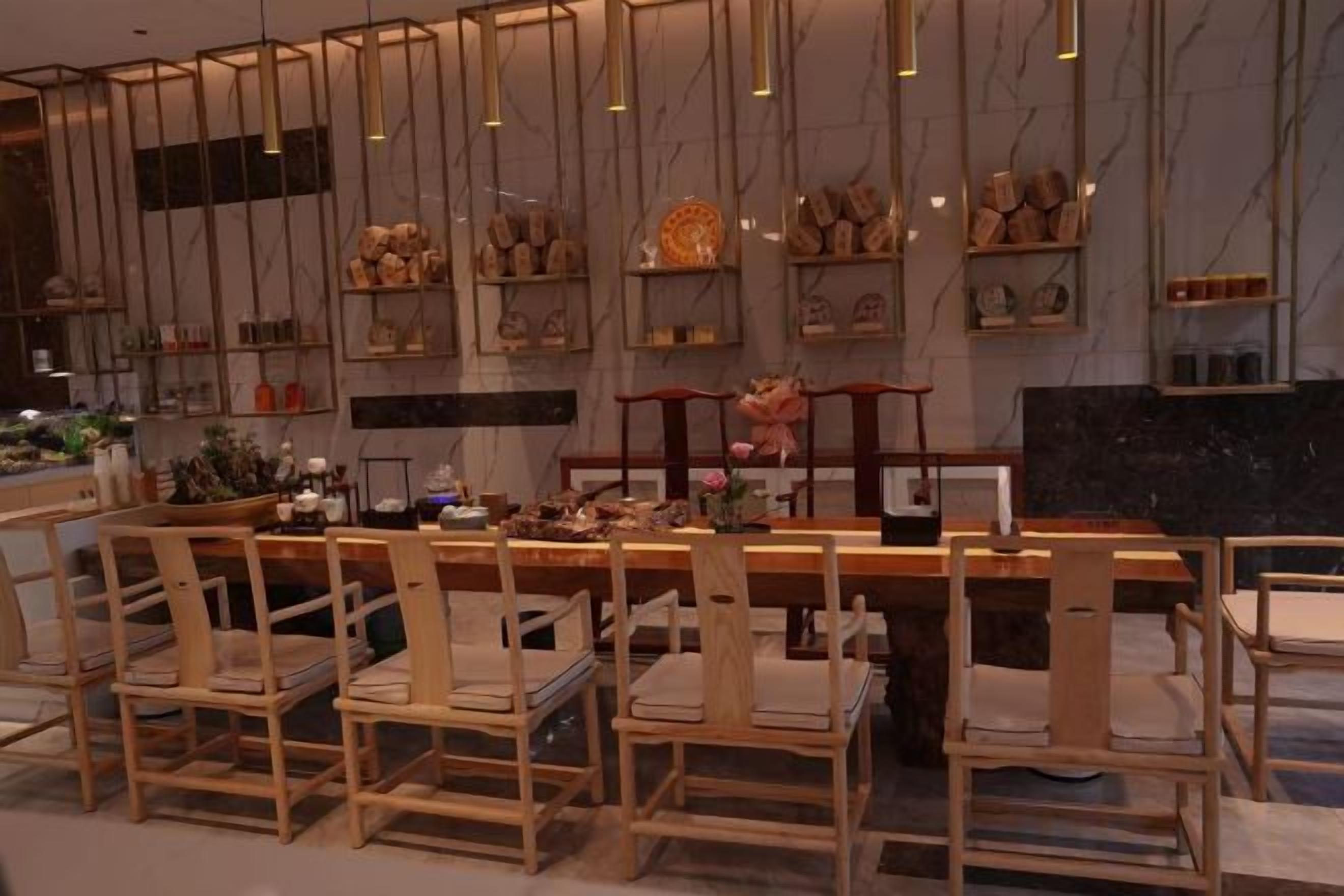 Un restaurante con una barra larga, sillas de madera y una pared de mármol con estantes que exhiben diversos artículos.