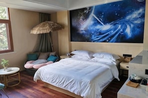 A bedroom with a large bed, a nightstand, a wall art depicting a cosmic scene, a window, and a small round table with a plant. - Pu'erbaiyuan Boutique Hotel (Pu'er)