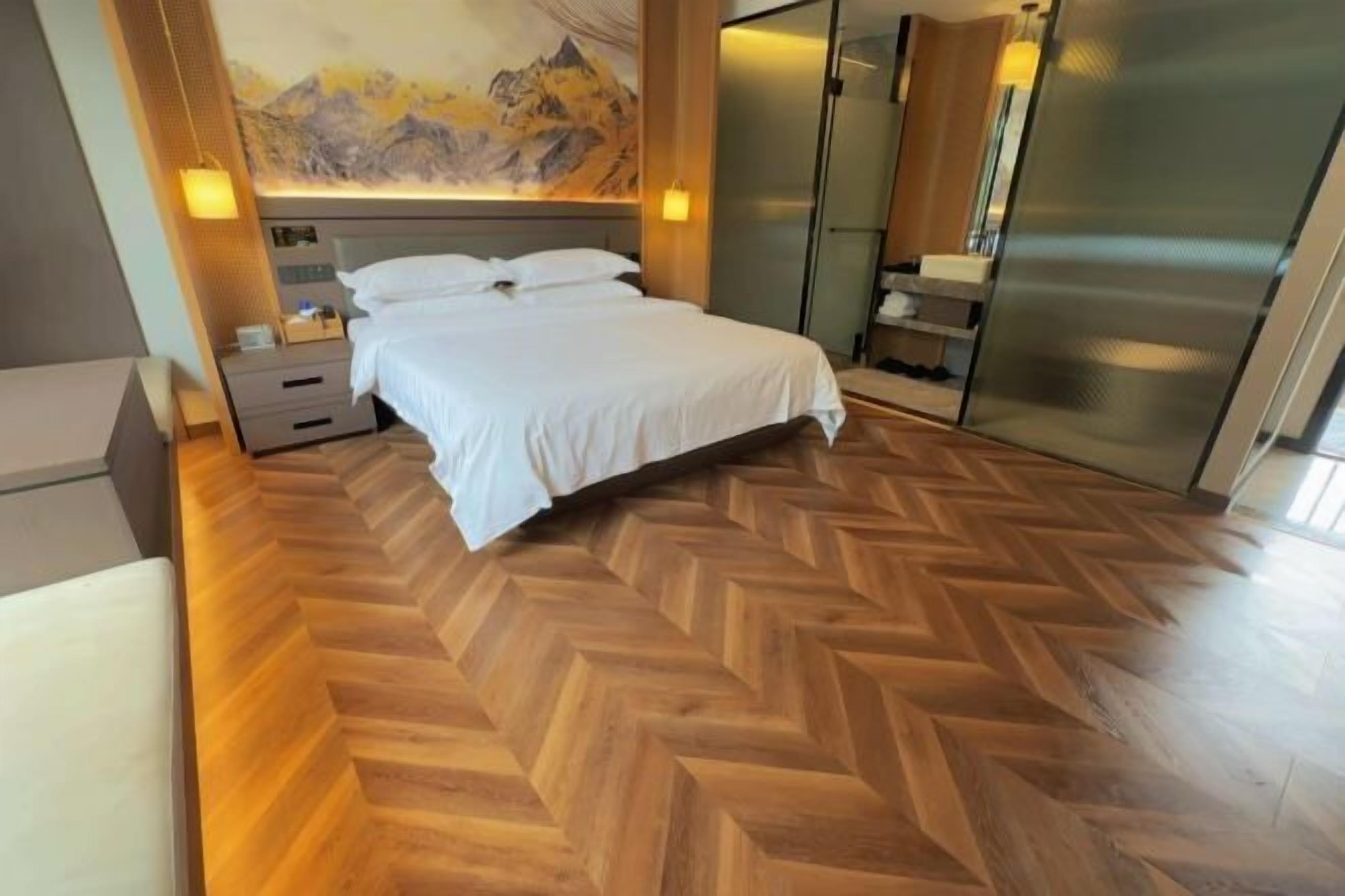 Quarto de hotel moderno com cama grande, piso de madeira em padrão losango, pintura de montanhas na parede e box de vidro.