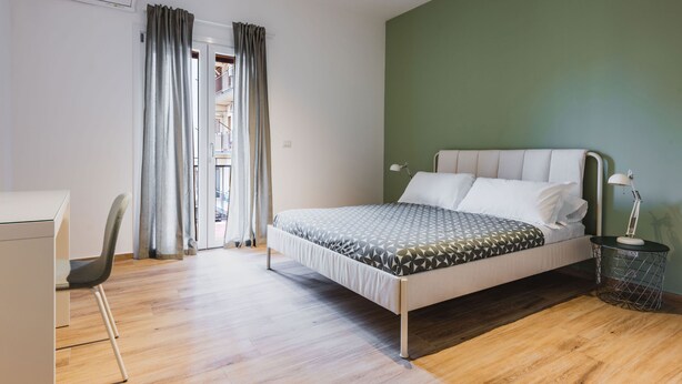 A bedroom with a bed, a desk, a chair, and a window with curtains. - Casa Eleonora con Balcone by Wonderful Italy (Catania)