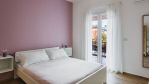 A bedroom with a bed, a nightstand, a window with curtains, and a view of the outside. - Casa Eleonora con Balcone by Wonderful Italy (Catania)