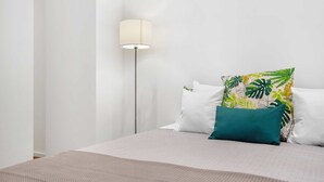 A bedroom with a bed, a floor lamp, and a tropical-themed pillow. - Funchal Tropical - Filodendro by Homie (Funchal)