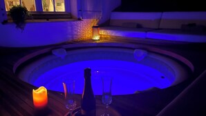 Un bain à remous avec un éclairage bleu, une bougie et deux verres posés sur une table en bois.