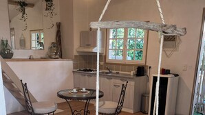 Une cuisine chaleureuse avec un fauteuil suspendu, une table à manger avec des chaises et une petite table ronde agrémentée d’une plante.