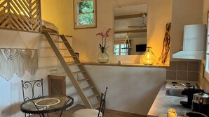 Une cuisine compacte dotée d’un plan de travail en bois, d’une cuisinière intégrée et d’un petit coin repas avec une table en verre et des chaises en métal.