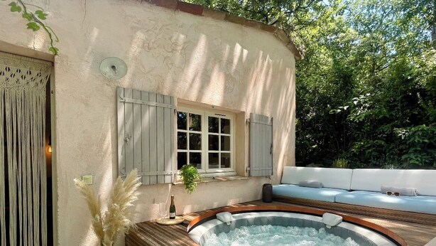 Un bain à remous dans un cadre extérieur rustique, avec une terrasse en bois et un mur blanc.
