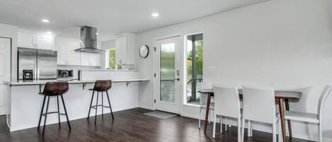 A modern kitchen with white cabinets, stainless steel appliances, and a bar area with stools.