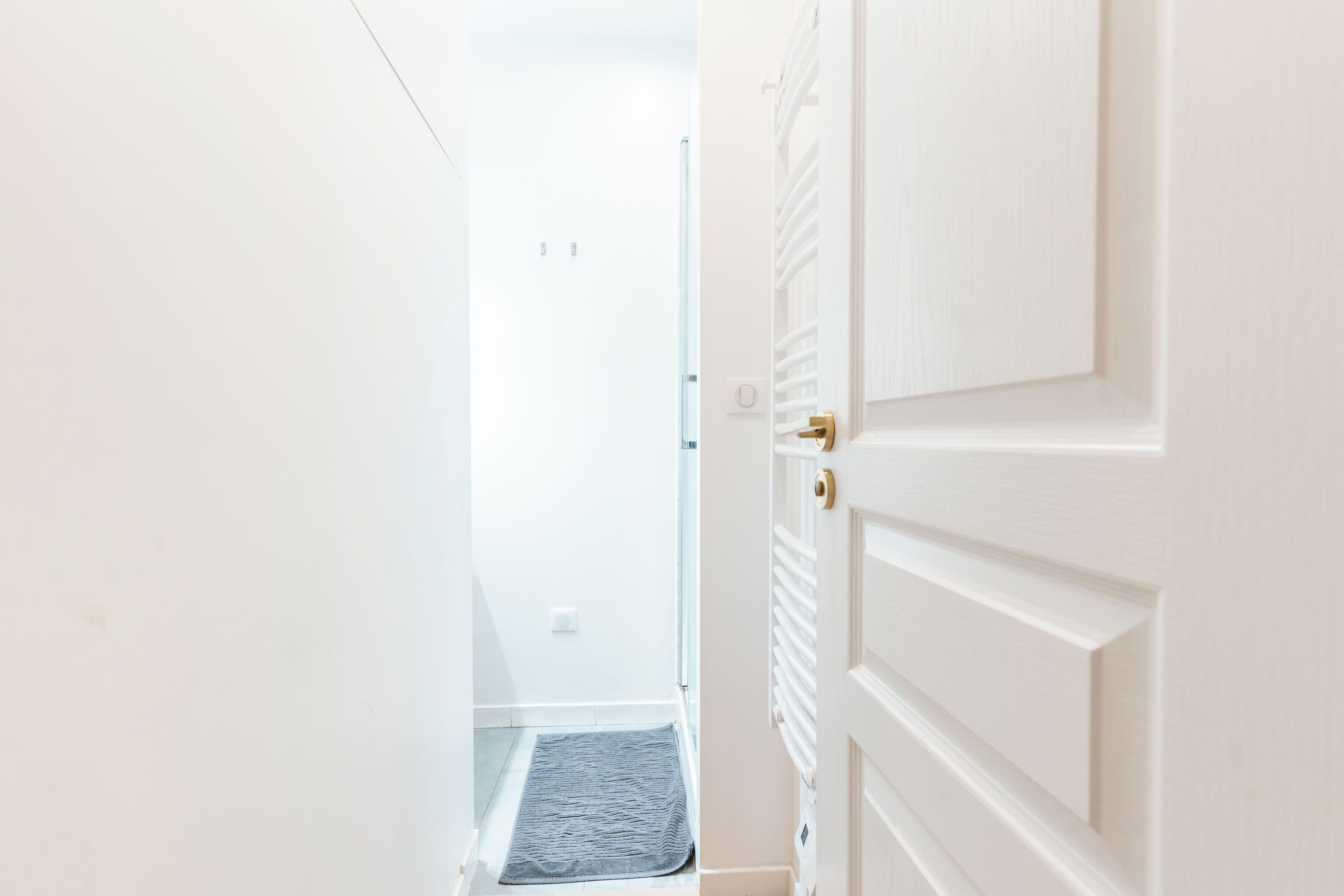 A hallway with a white door, a small rug, and a light switch on the wall.