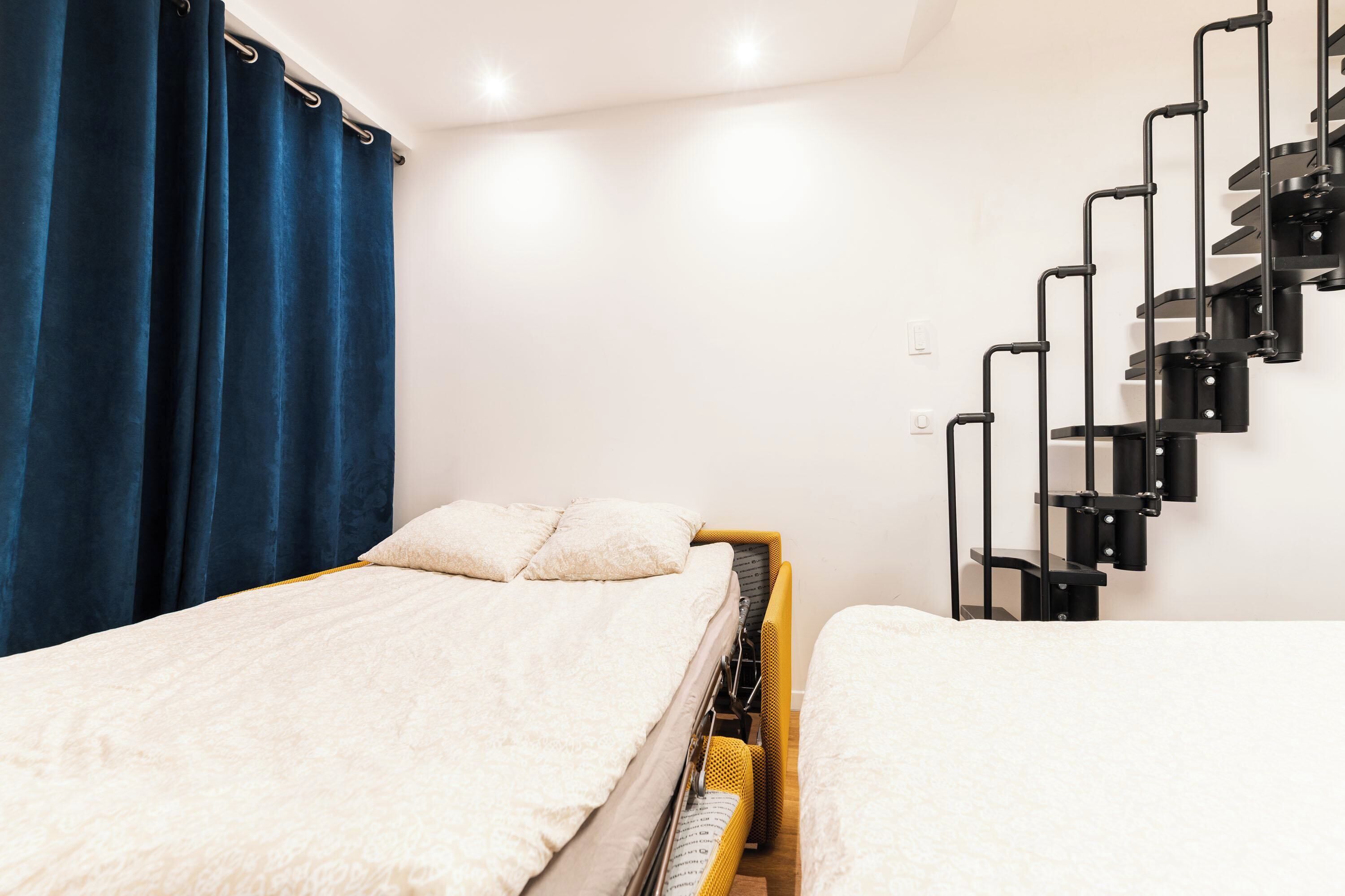 Une chambre avec deux lits, un escalier et une fenêtre avec des rideaux.