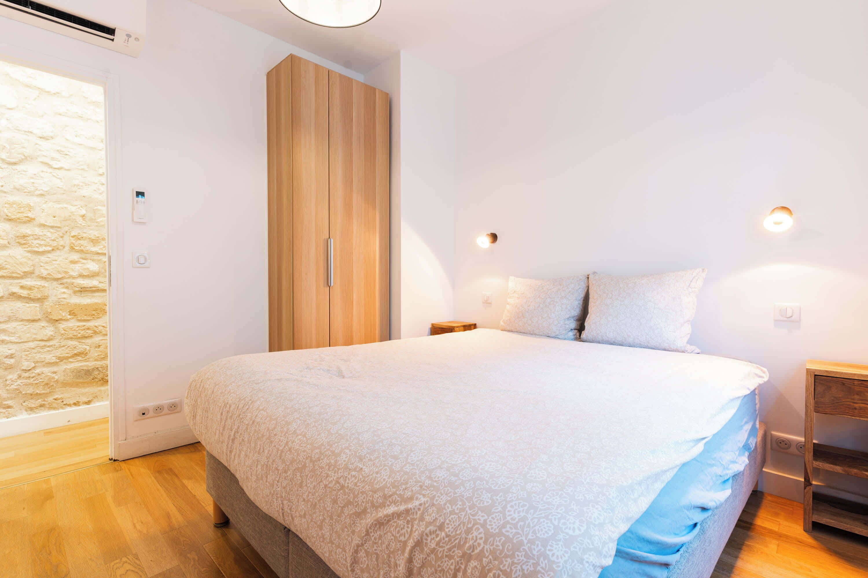 A bedroom with a bed, wooden wardrobe, and a stone wall.