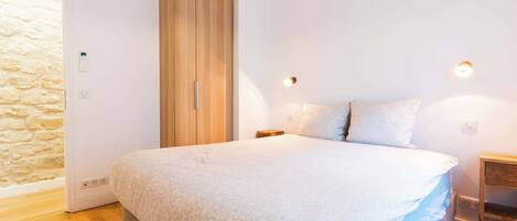 A bedroom with a bed, wooden wardrobe, and a stone wall.