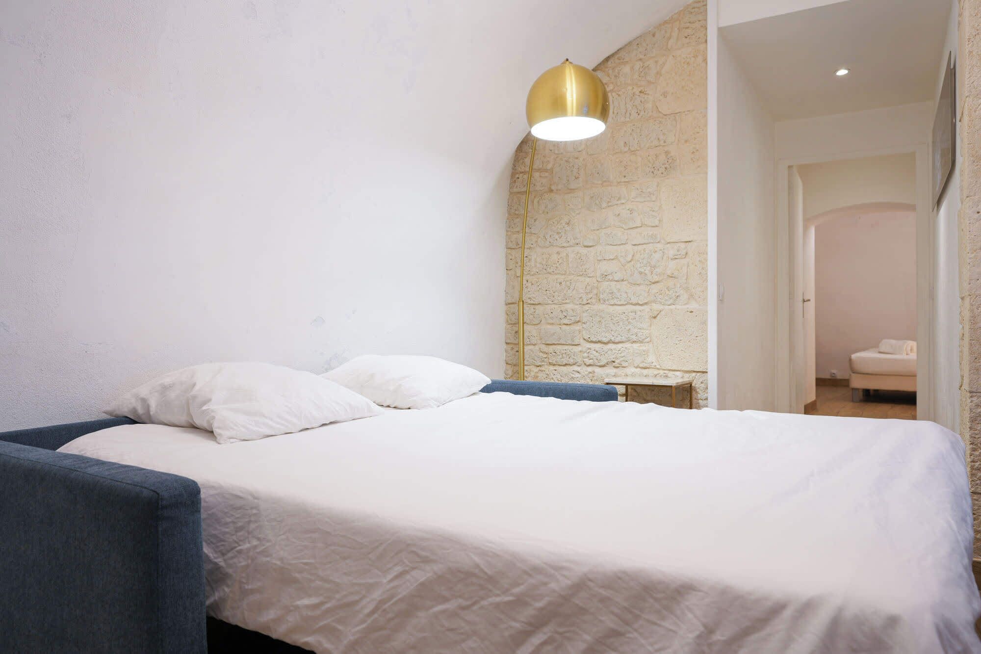 A bedroom with a bed, white pillows, a blue headboard, and a stone wall.